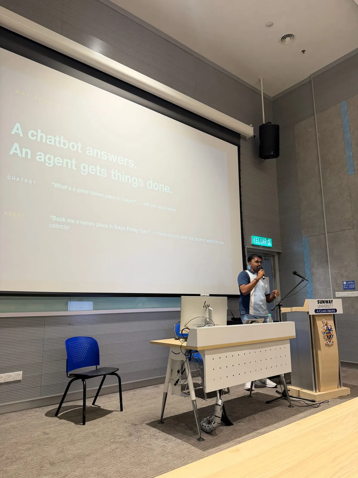 Slide reading 'A chatbot answers. An agent gets things done.' on the lecture theatre screen